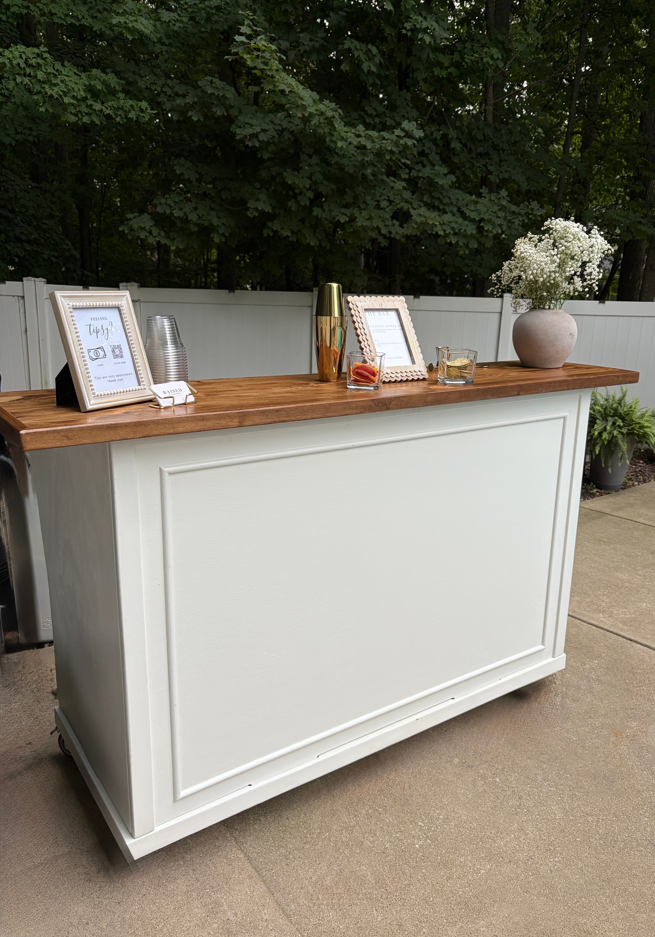 White mobile bar with wood top, gold cocktail shaker, and baby's breath floral arrangement